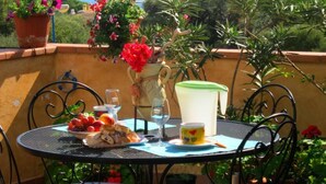 Ein runder Metalltisch mit Stühlen, eine Fruchtschale, eine Kanne, ein Glas und eine Tasse auf einer Terrasse mit Meerblick.