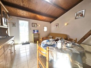 A cozy room with a wooden ceiling, a dining table set with tea cups and a kettle, a sofa with cushions, and a television on a stand.