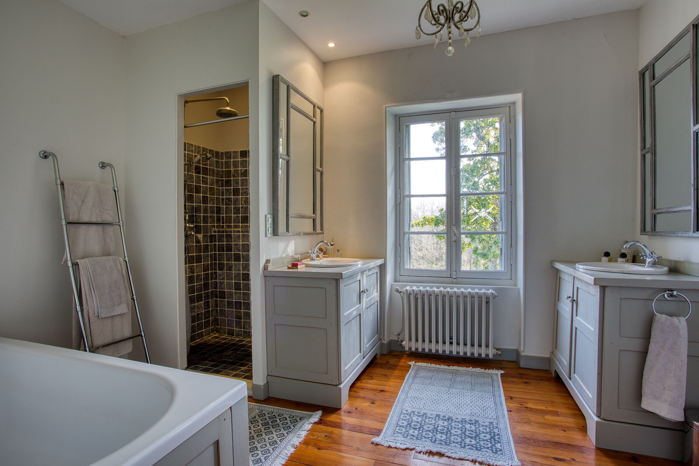 A bathroom with a shower, two sinks, a radiator, and a window with a view.
