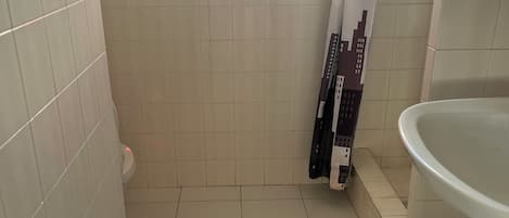 A bathroom with white tiled walls, a window with red curtains, a toilet, and a sink.
