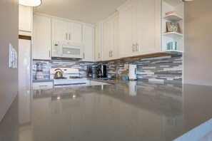 A modern kitchen with white cabinets, a stainless steel range, a microwave, and a tiled backsplash.