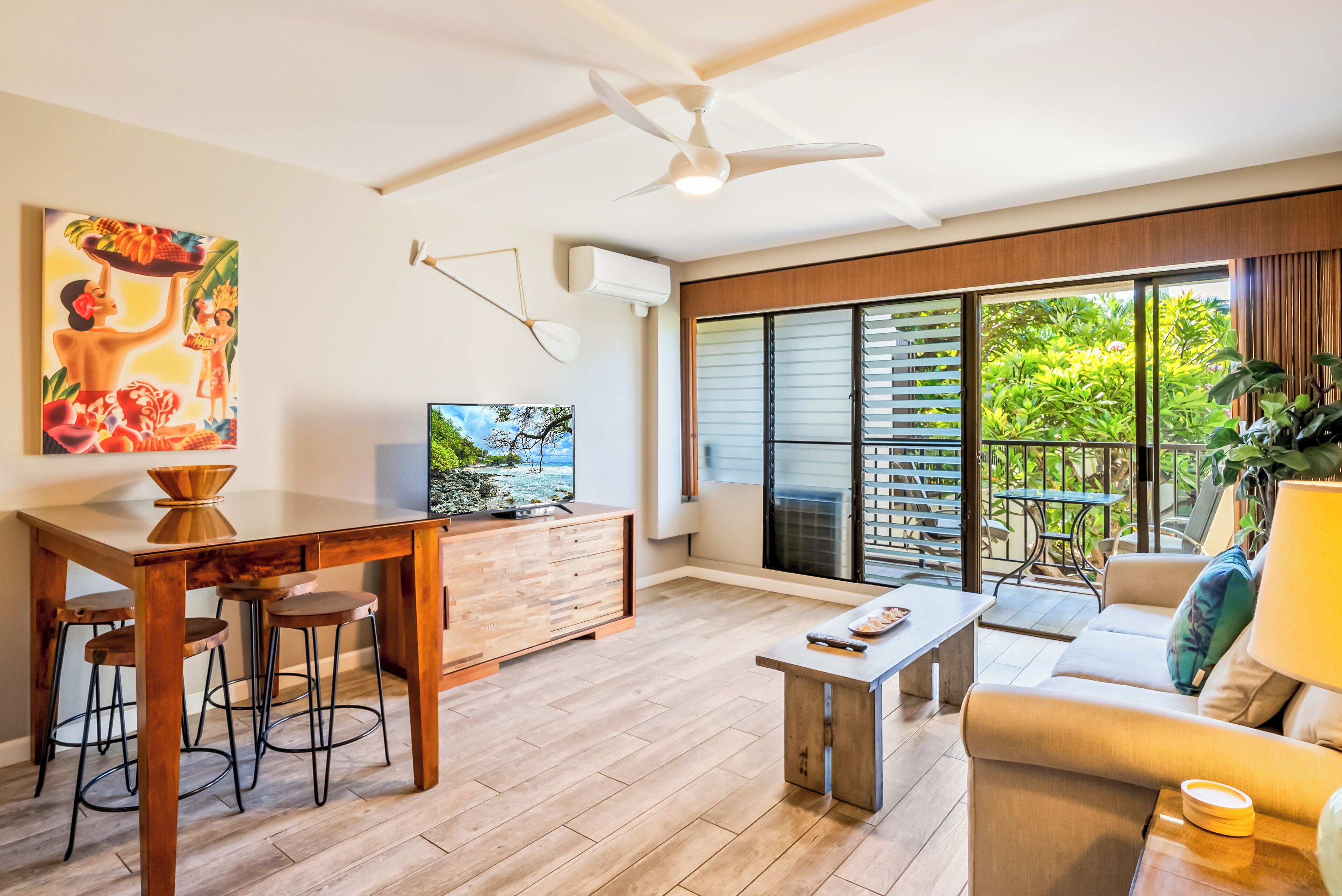 A modern living room with a wooden dining table, bar stools, a sofa, and a TV.