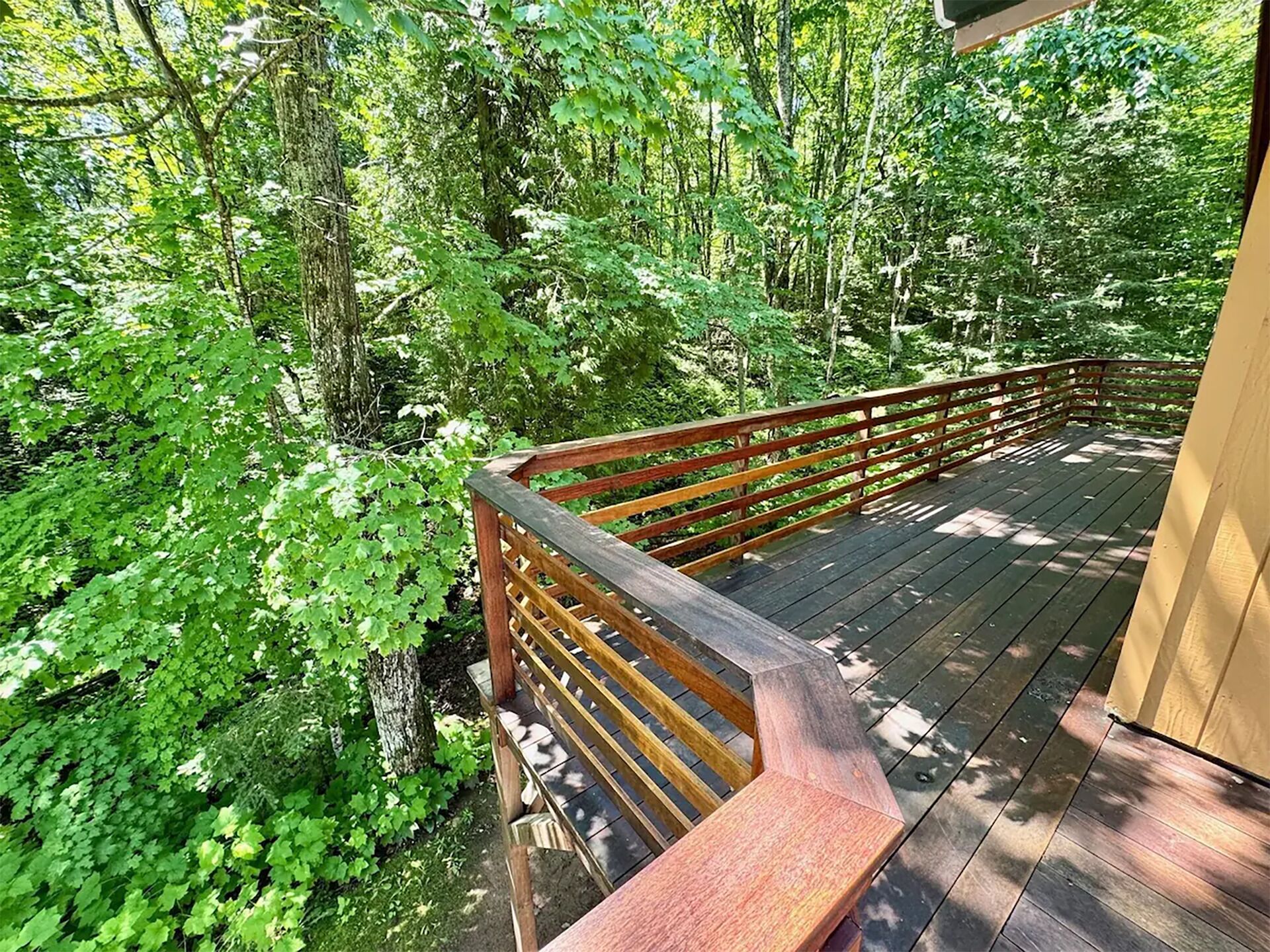 A wooden deck with a railing overlooking a forested area.