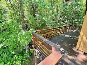 A wooden deck with a railing overlooking a forested area.