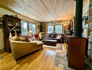 A cozy living room with a fireplace, wooden floors, and large windows.