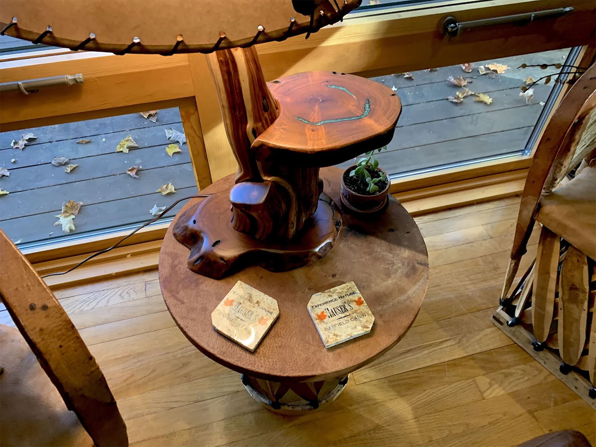 Una mesa de madera con dos libros, una planta pequeña en maceta y una ventana con hojas otoñales.