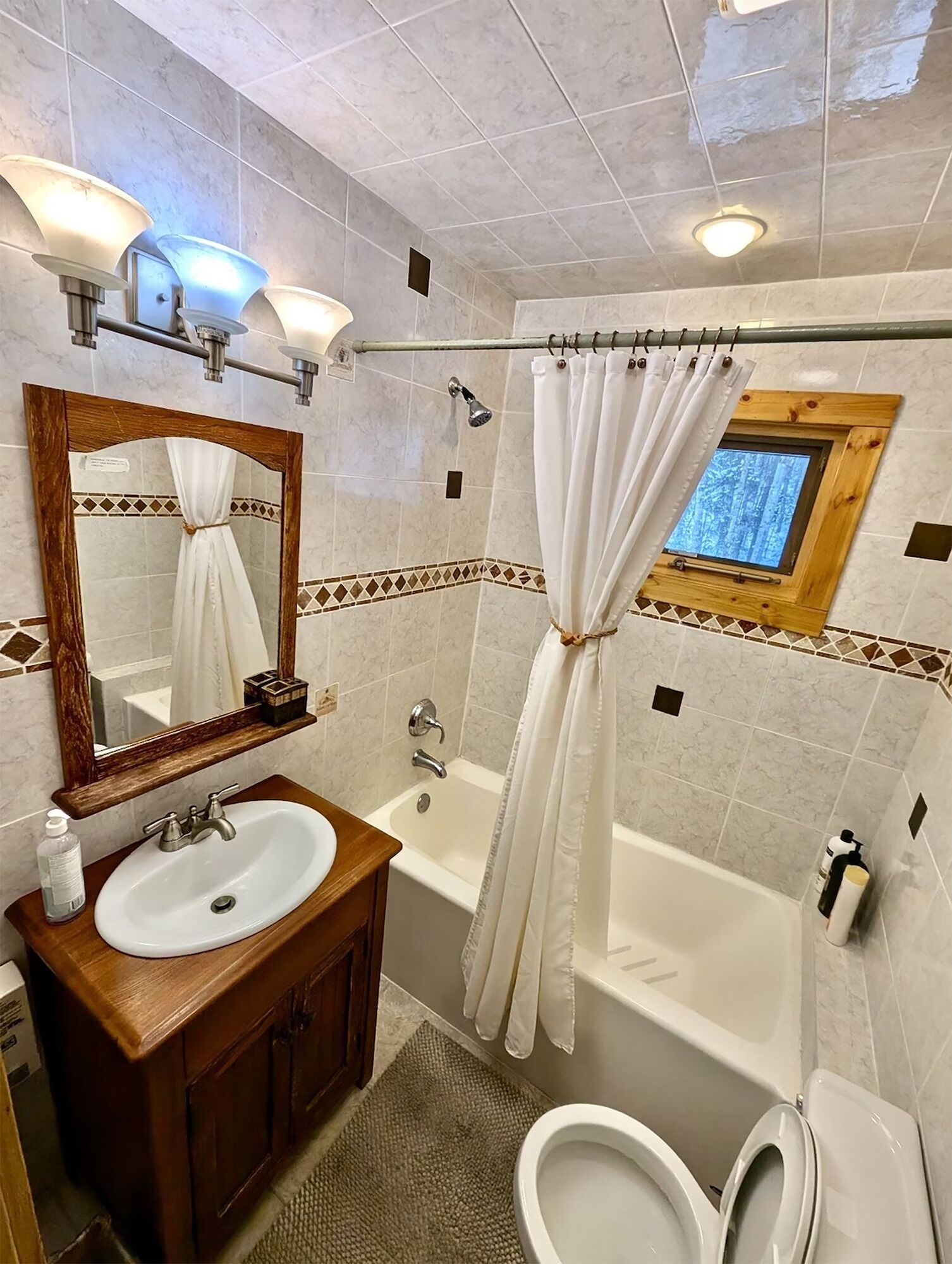 A bathroom with a wooden vanity, a bathtub, a shower, a toilet, and a mirror with lights.