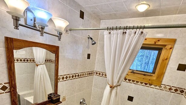 A bathroom with a wooden vanity, a bathtub, a shower, a toilet, and a mirror with lights.