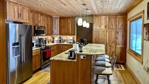 A kitchen with wooden cabinets, stainless steel appliances, a granite countertop, and a bar stool.