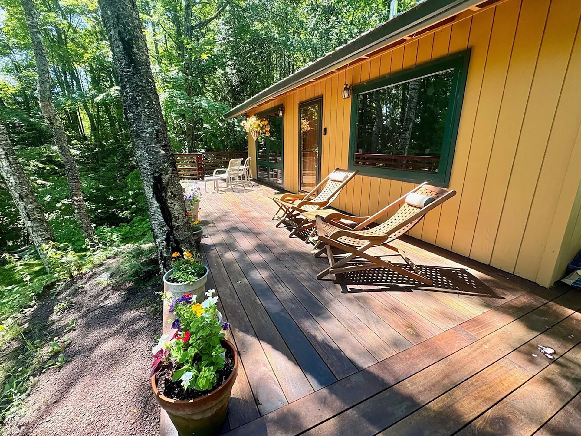 Une terrasse en bois avec des chaises longues, un pot de fleurs et un bâtiment doté de grandes fenêtres.
