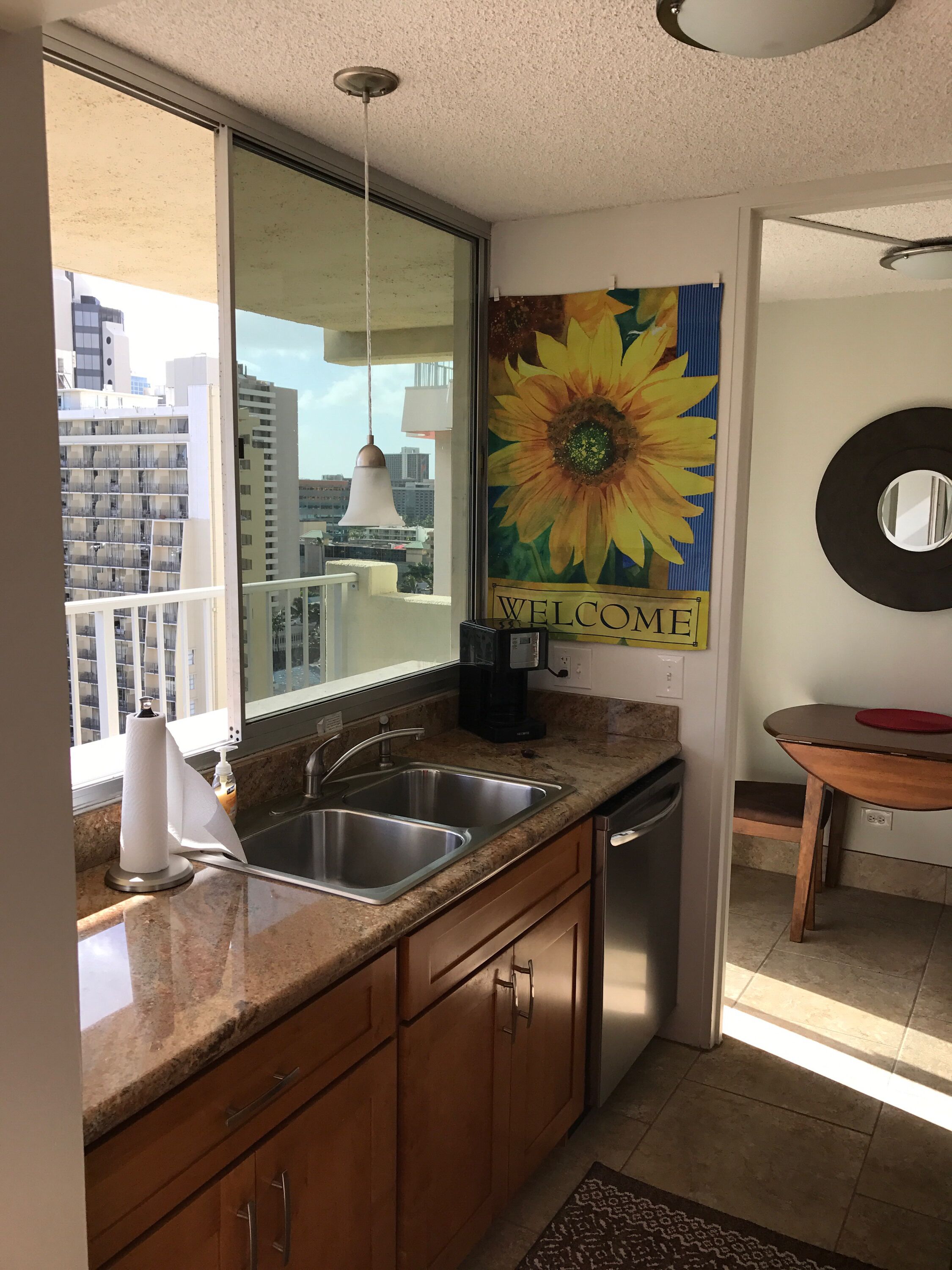A kitchen with a sink, countertop, and wooden cabinets. There is a window with a view of buildings outside.