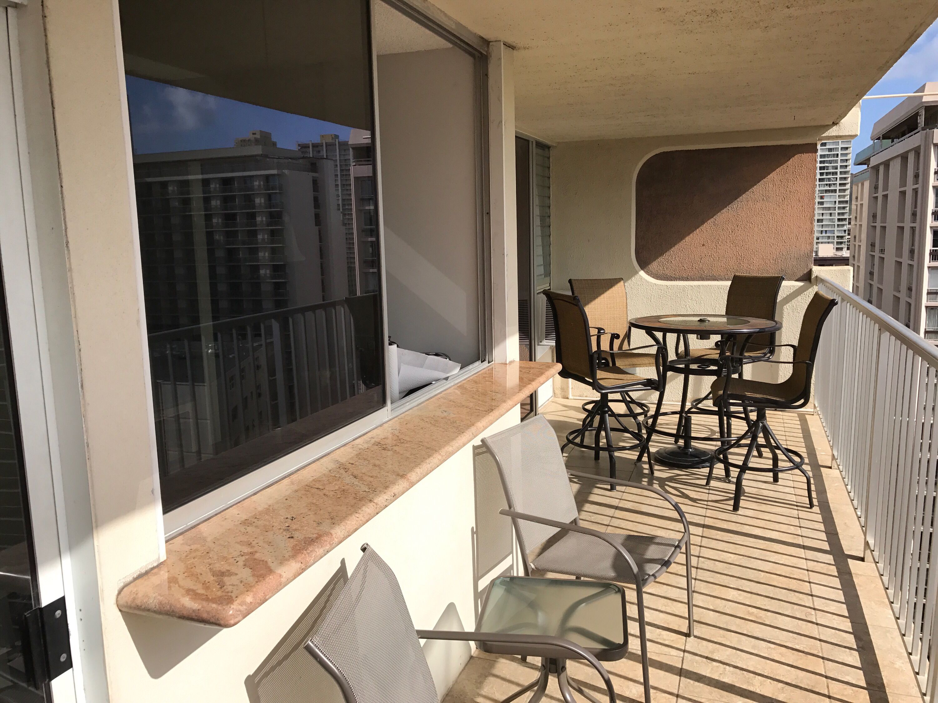 A balcony with a table and chairs, a window with blinds, and a view of buildings.