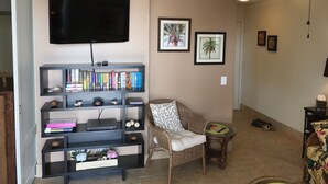 Ein Wohnzimmer mit Flachbildfernseher, Bücherregal, Korbsessel und kleinem Tisch.