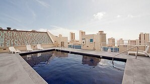 Ein Pool auf dem Dach mit klarem, blauem Wasser, umgeben von Liegestühlen und Blick auf die Stadt.