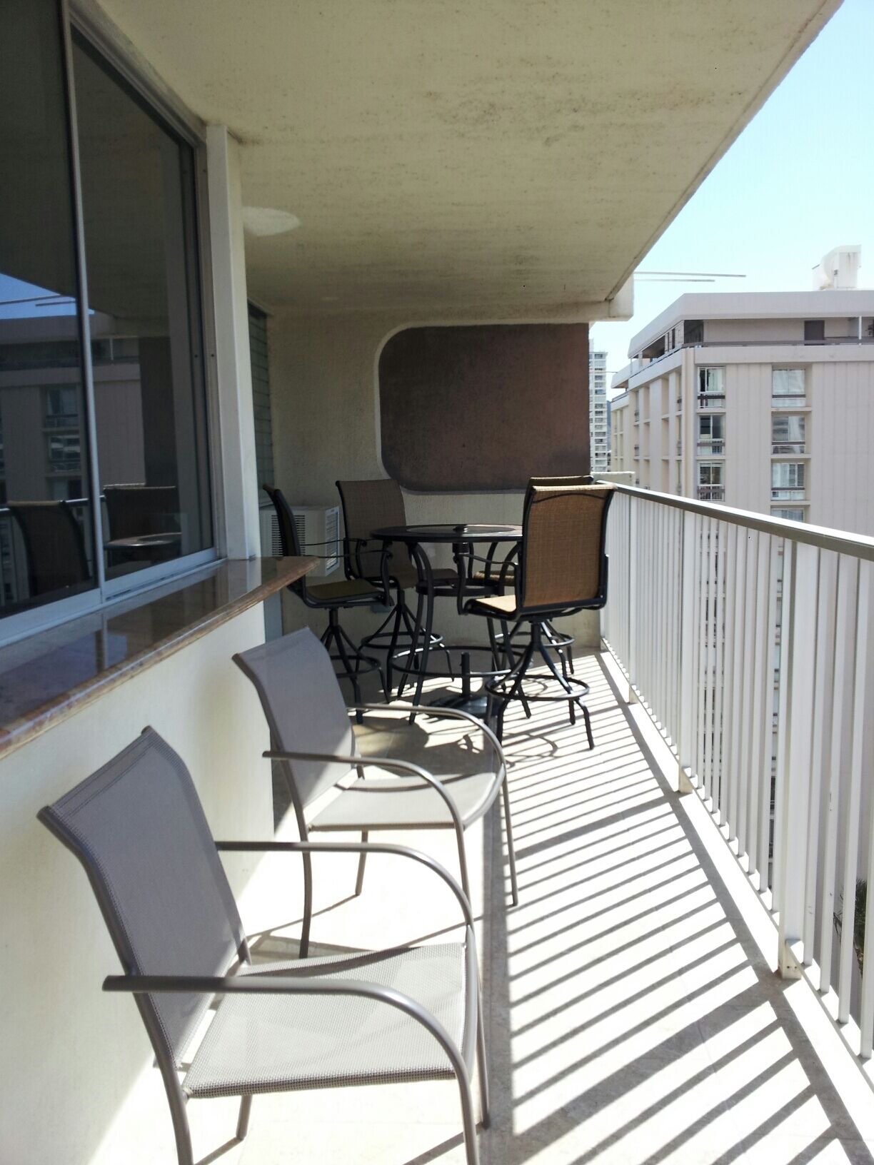 A balcony with a table and chairs, a view of buildings, and a railing.