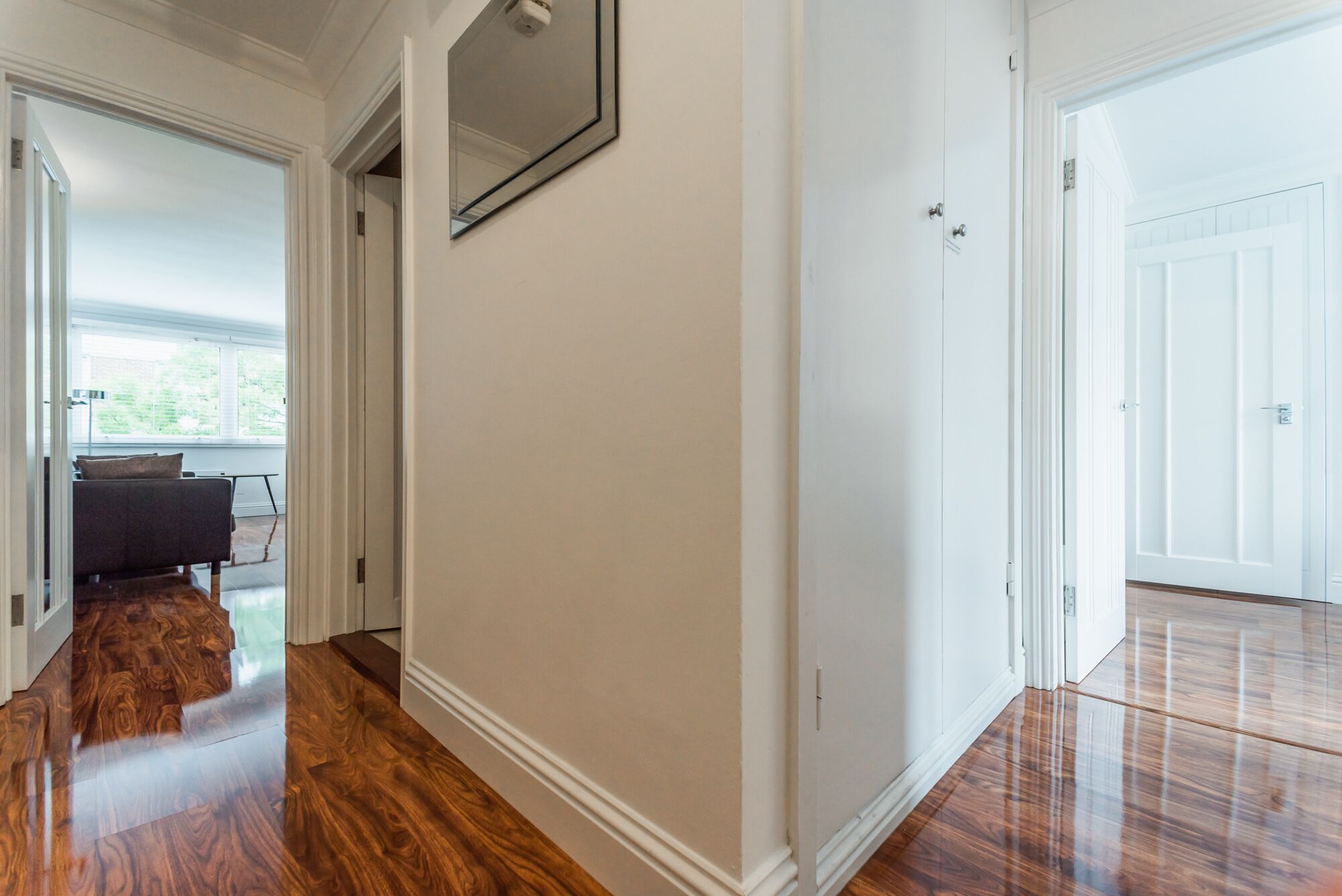 A hallway with wooden flooring, white walls, and a door leading to another room.