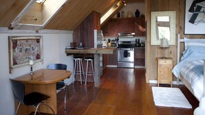 A compact kitchen with a central island, a dining area with a table and chairs, and a bedroom with a bed and nightstand. - ROMANTIC,ARTIST'S PVT 'FOREST SUITE', 5 ac.Redwds,trail, NEW OD SHR, Mendo 2 mi. (Mendocino)