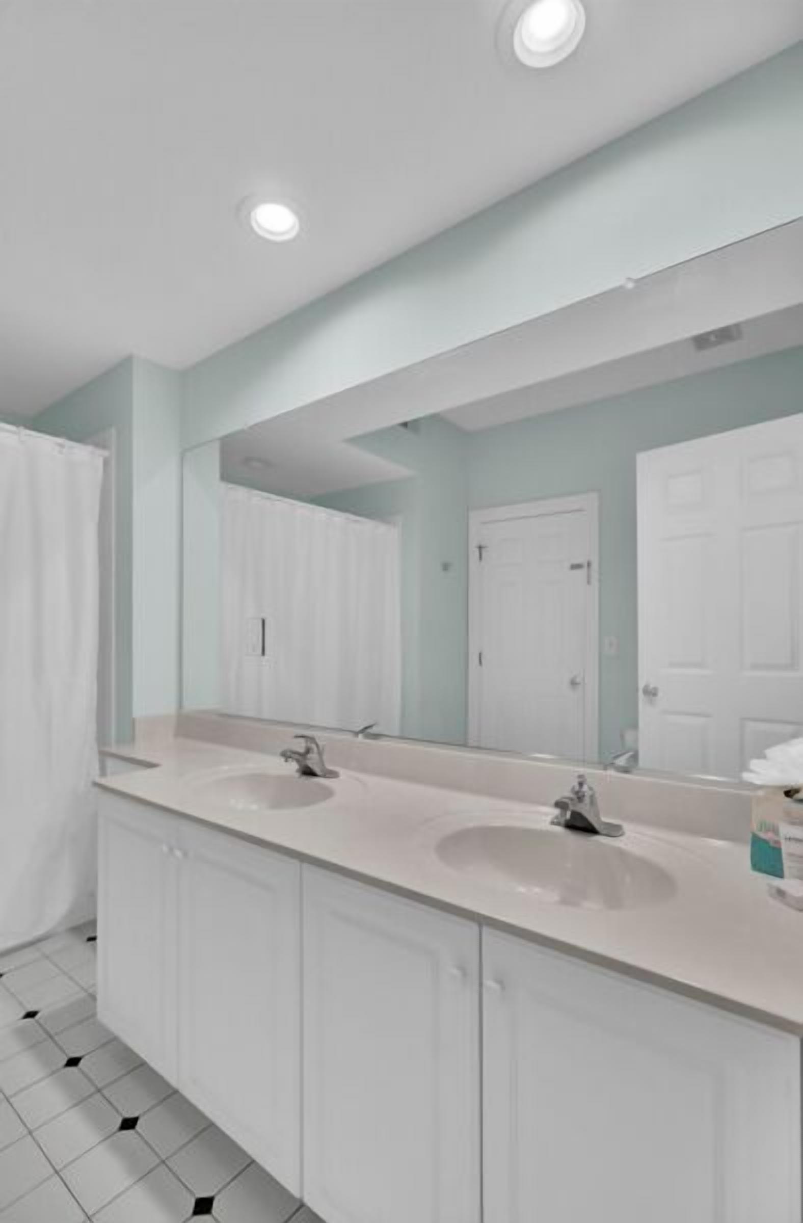 A modern bathroom with two sinks, a large mirror, and a shower curtain.