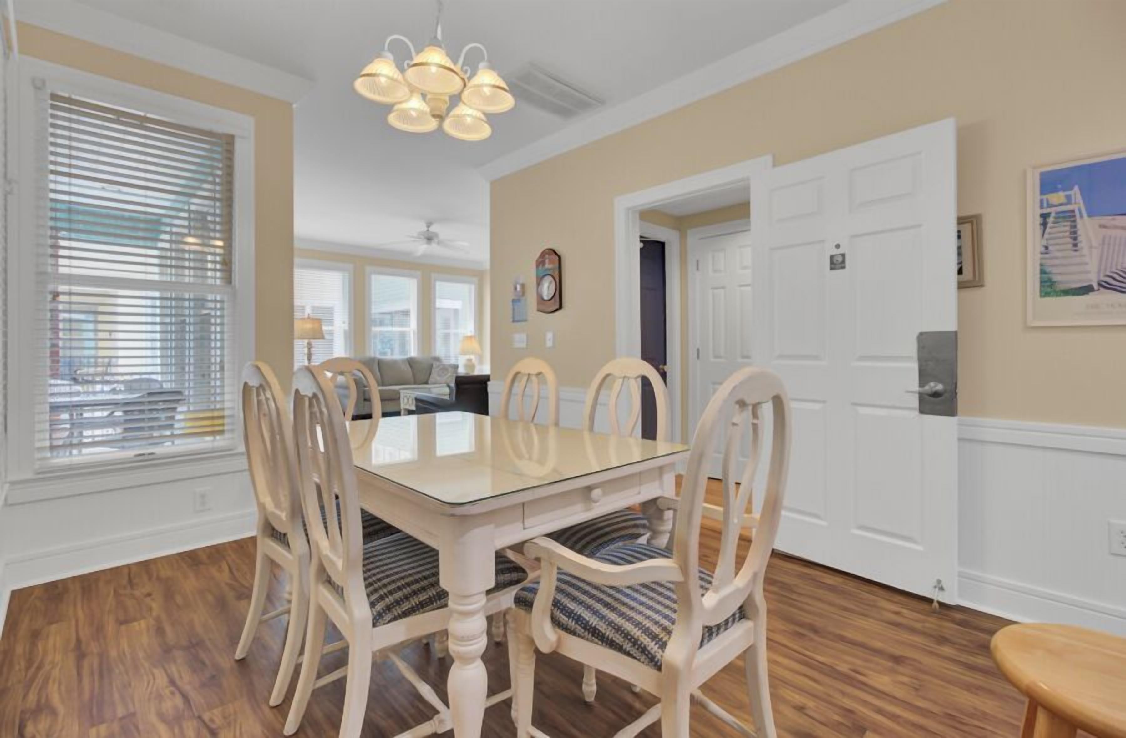 A dining area with a glass-top table, white chairs, and a chandelier.