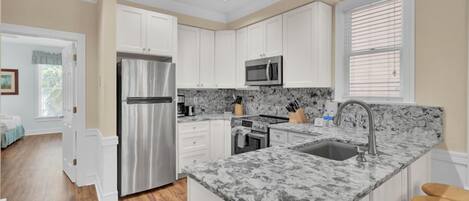 Una cocina moderna con armarios blancos, un refrigerador de acero inoxidable, un microondas y una encimera de mármol.
