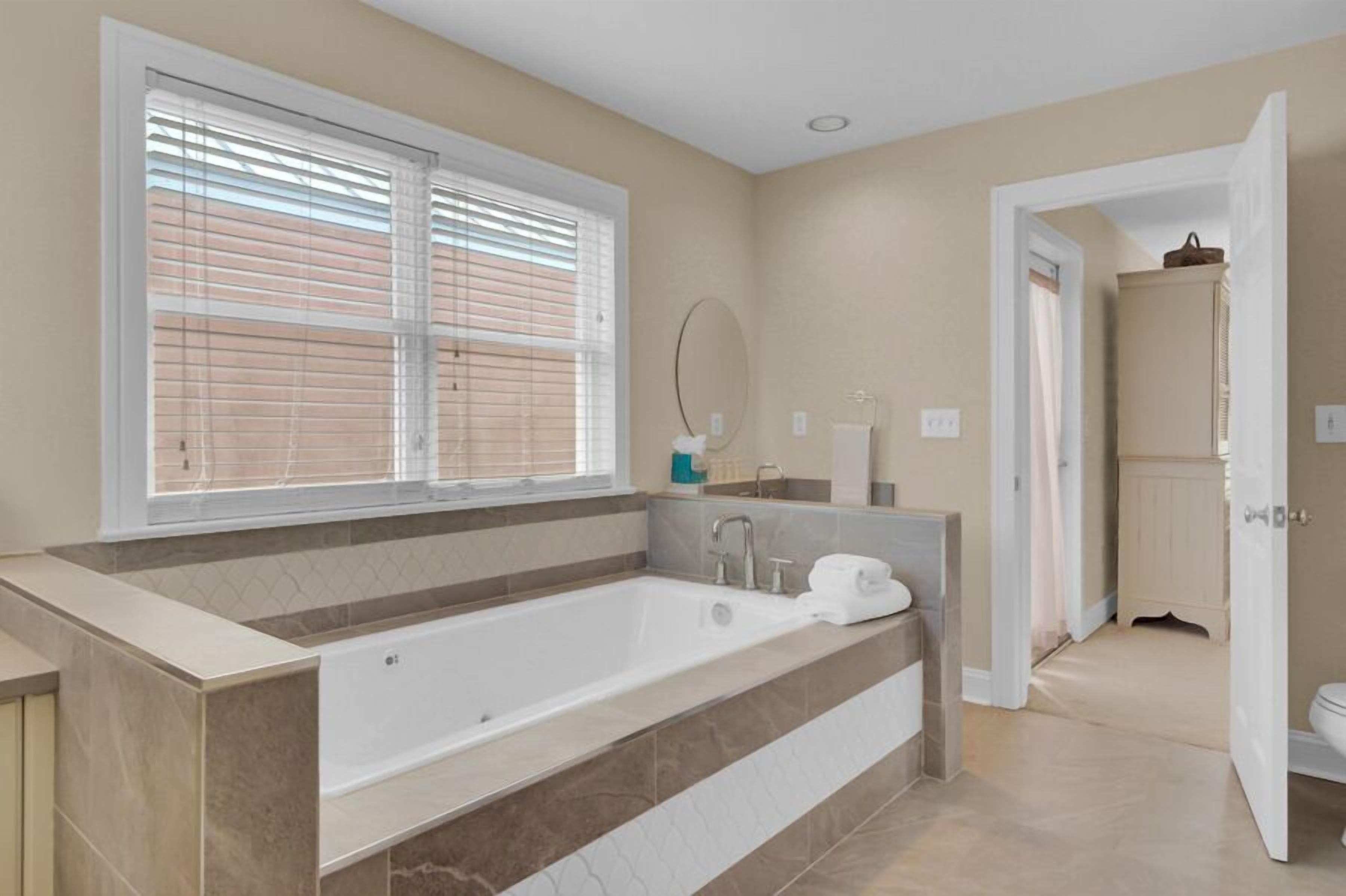 A modern bathroom with a large bathtub, a vanity with a mirror, and a toilet visible through an open door.