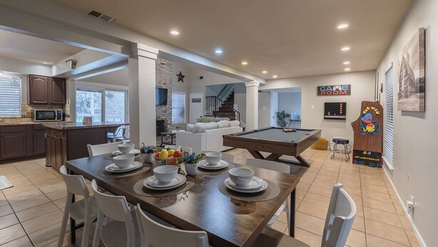 A spacious living area with a dining table set for four, a pool table, and a kitchen area with dark cabinets and a microwave. - Private Pool, Mini Golf, Game Room & Fire Pit near Six Flags (San Antonio)