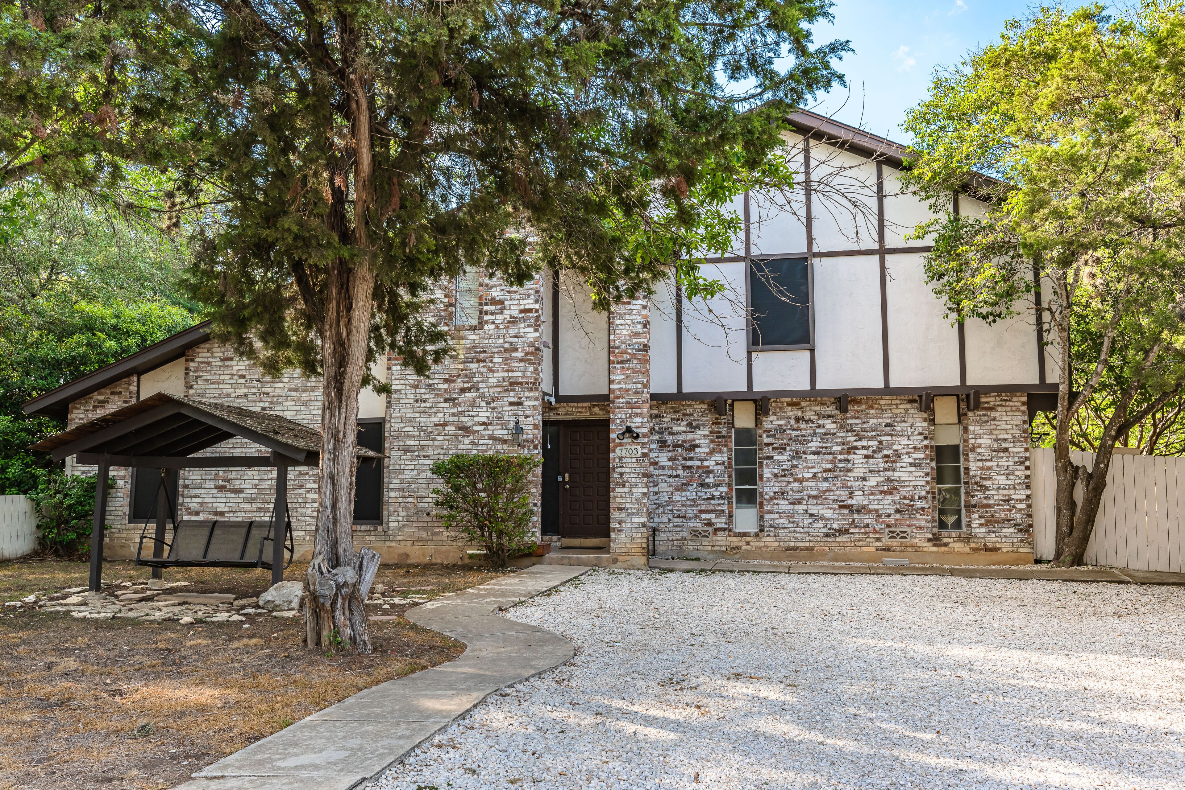 Une maison à deux étages avec une façade en briques, un porche couvert et une allée gravillonnée.