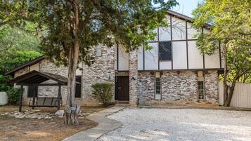 Une maison à deux étages avec une façade en briques, un porche couvert et une allée gravillonnée.