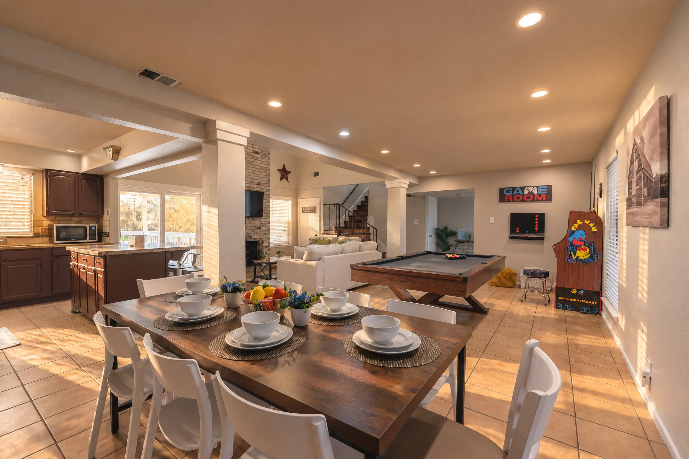 A spacious dining area with a pool table, a kitchen with modern appliances, and a living area with a staircase.