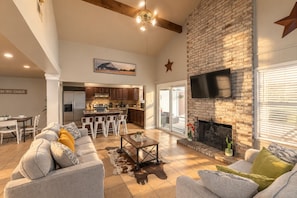 A spacious living area with a fireplace, a dining area, and a kitchen with a large island. - Private Pool, Mini Golf, Game Room & Fire Pit near Six Flags (San Antonio)