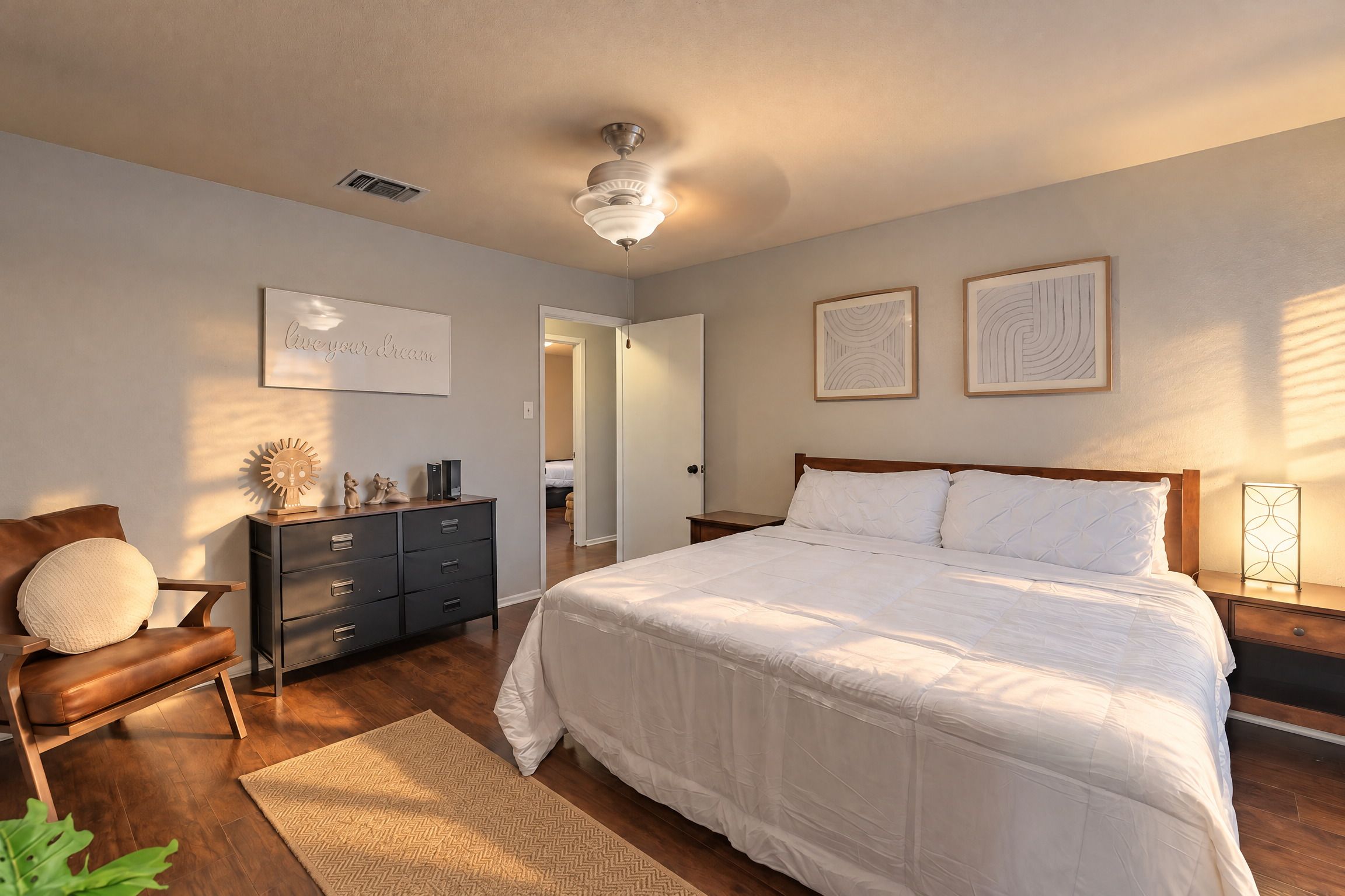 A bedroom with a bed, dresser, chair, and artwork on the walls.