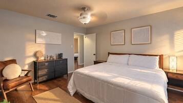 A bedroom with a bed, dresser, chair, and artwork on the walls.