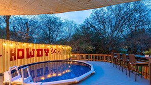 An outdoor swimming pool with a wooden deck, surrounded by trees and a deck with outdoor seating. - Private Pool, Mini Golf, Game Room & Fire Pit near Six Flags (San Antonio)