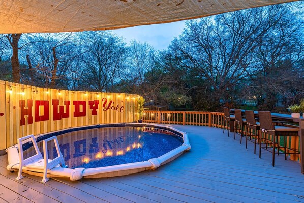 Piscina esterna con bordo in legno, circondata da alberi e da una terrazza con posti a sedere.