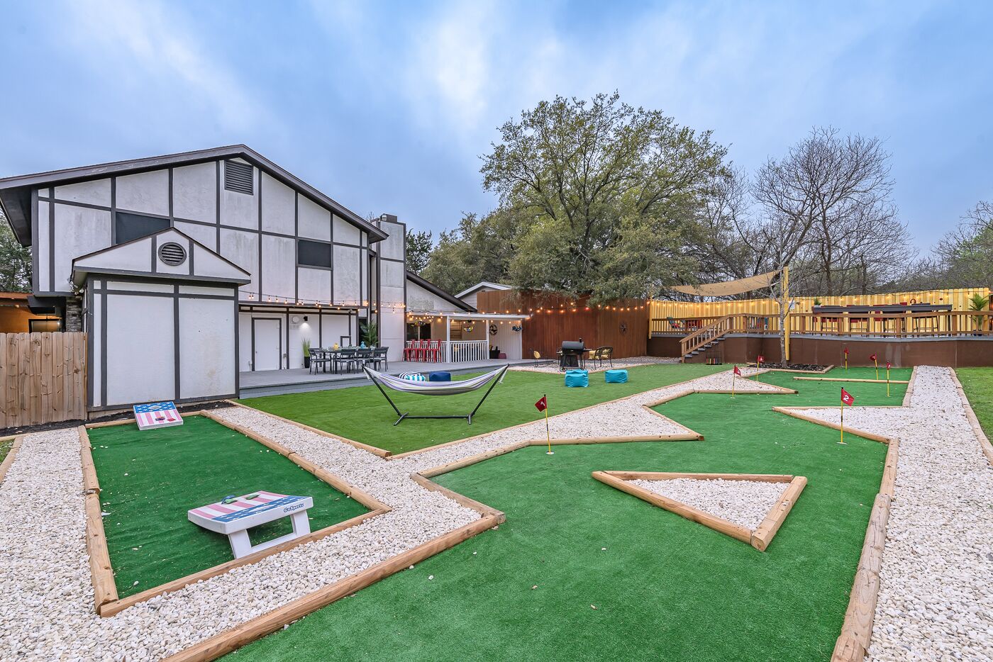 A modern house with a backyard featuring a putting green, a hammock, and a barbecue area.