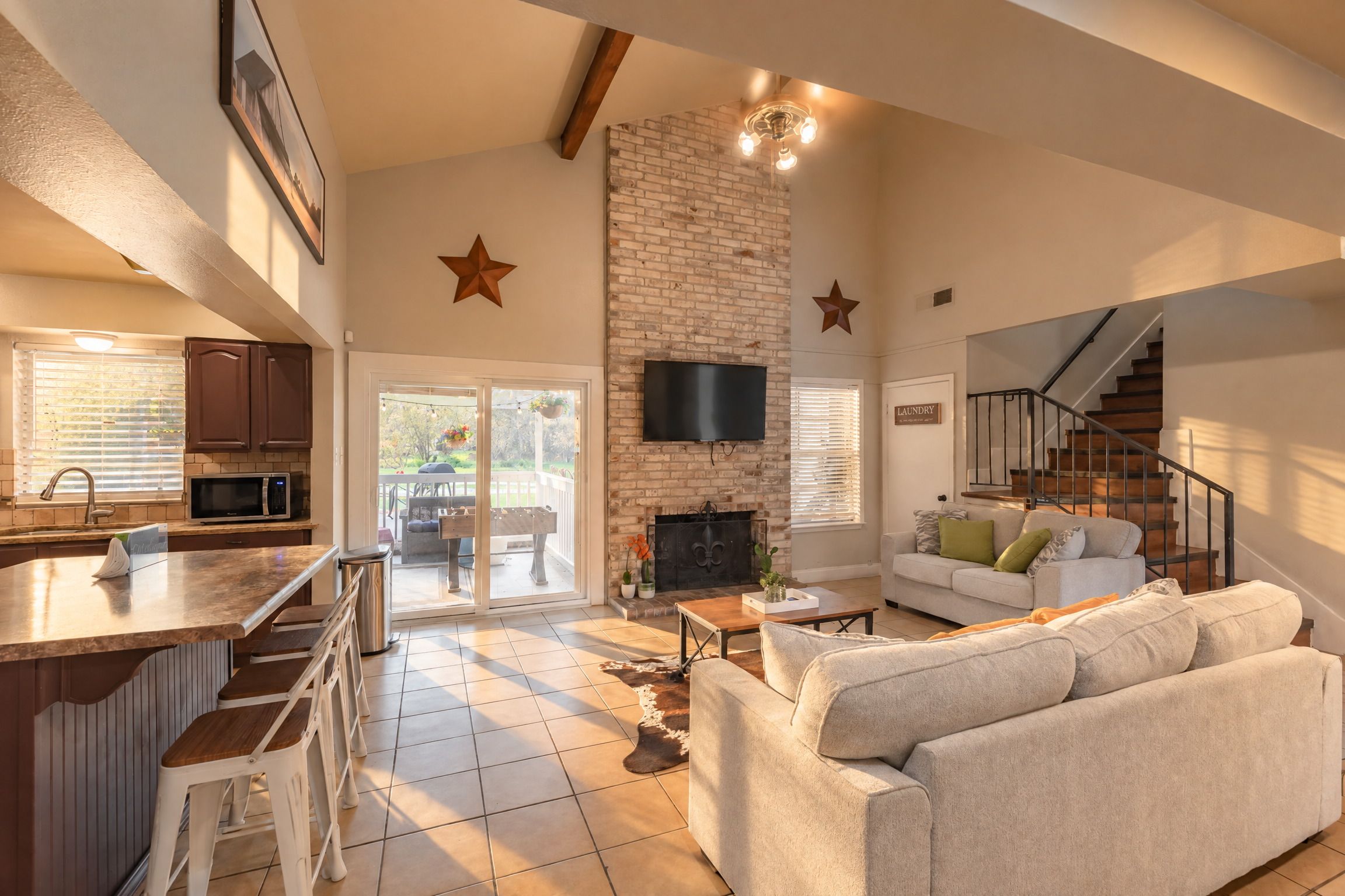A spacious living area with a fireplace, a kitchen with a bar, and a staircase leading to an upper level.