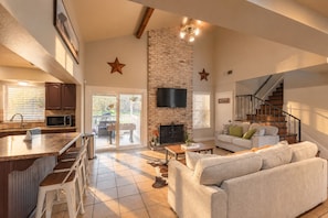 A spacious living area with a fireplace, a kitchen with a bar, and a staircase leading to an upper level. - Private Pool, Mini Golf, Game Room & Fire Pit near Six Flags (San Antonio)