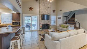 A spacious living area with a fireplace, a kitchen with a bar, and a staircase leading to another level. - Private Pool, Mini Golf, Game Room & Fire Pit near Six Flags (San Antonio)