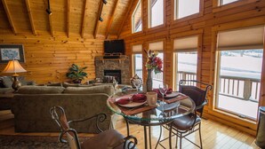 Een gezellig interieur van een chalet met een open haard, houten wanden, een eethoek met een glazen tafel en uitzicht op het besneeuwde landschap.