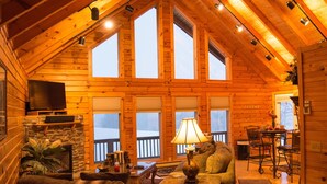 A cozy log cabin interior with a stone fireplace, a television, and a dining area with a table and chairs. - ✧King Cabin - find out why it is the KING! (Dryfork)