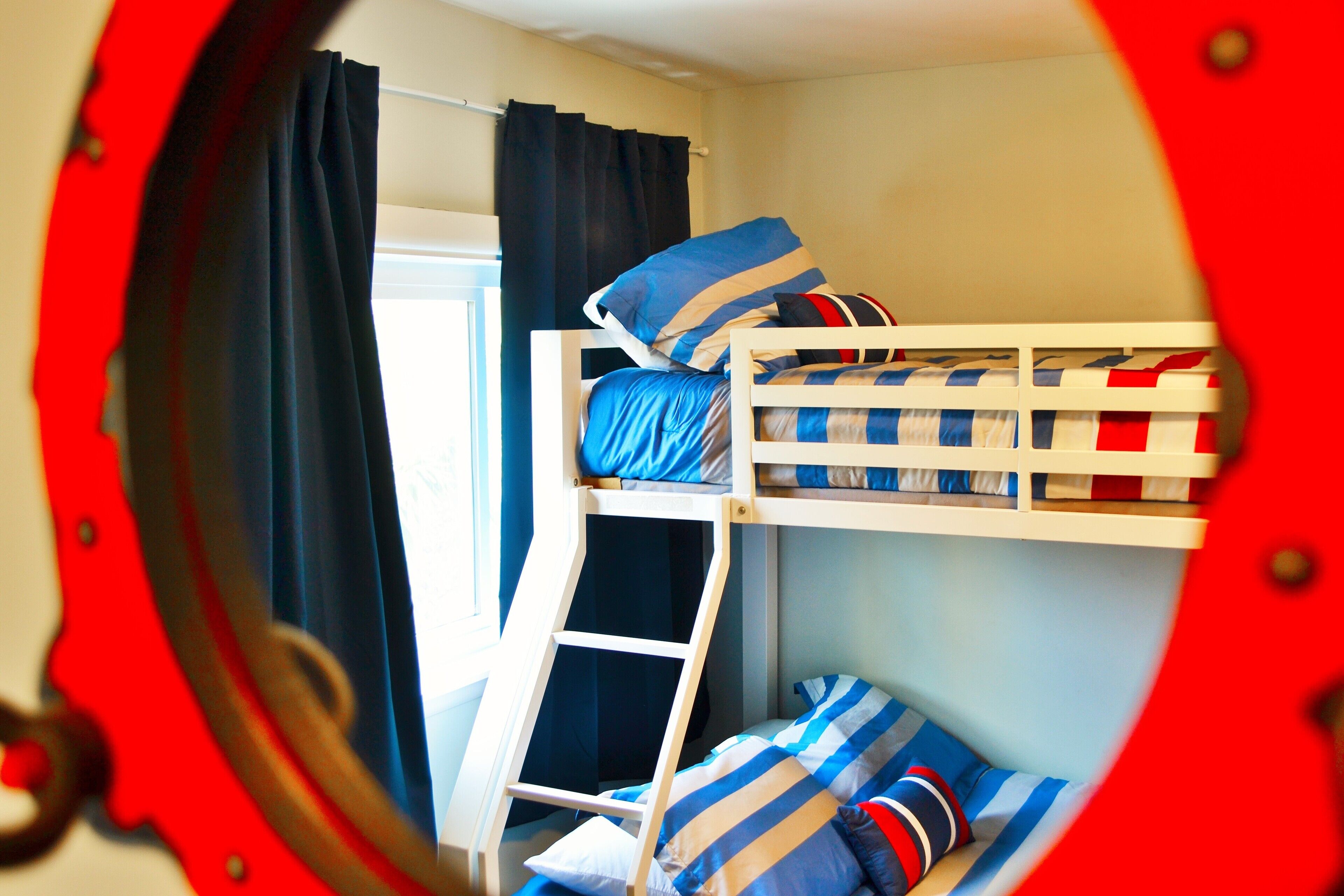 Une chambre avec un lit superposé, une échelle, une fenêtre avec des rideaux et un cadre de fenêtre circulaire.