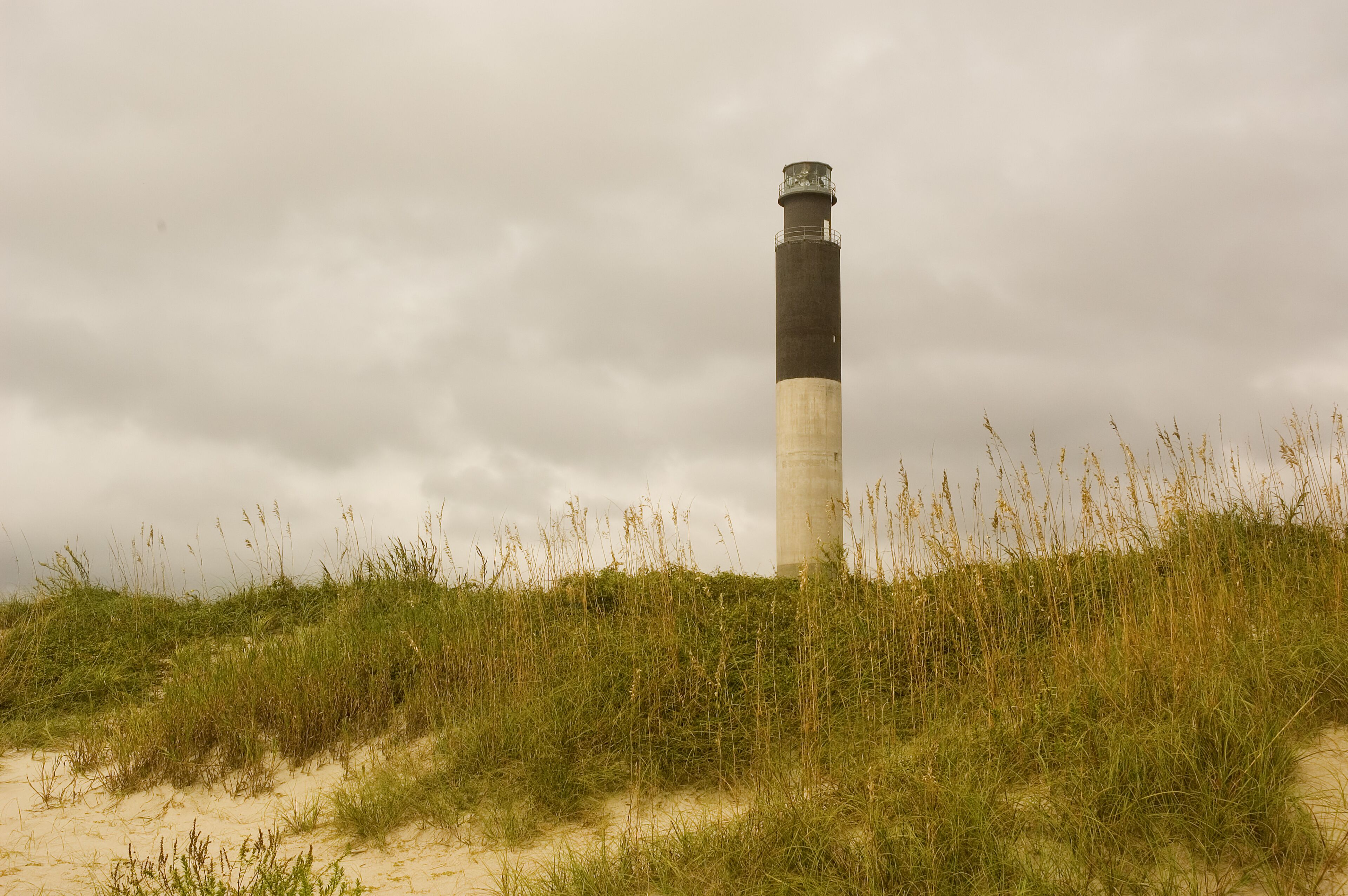 Un faro en una duna arenosa con hierba alta, bajo un cielo nublado.