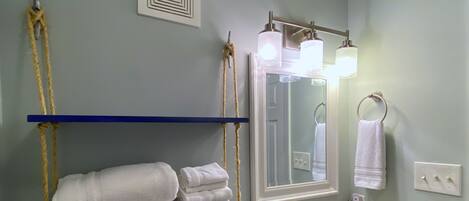 A bathroom with a white sink, a mirror with lights, and towels on blue shelves.