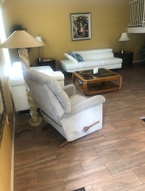 Cozy living room with a sofa, armchair, and coffee table, featuring a framed artwork and a lamp.