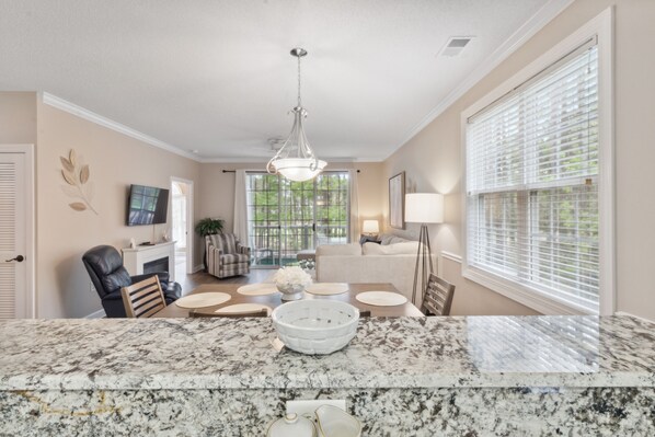 A modern kitchen with a marble countertop, a chandelier, and a dining area with a table and chairs. - River Crossing #1224- Gated Community! (North Myrtle Beach)