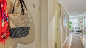 Un pasillo con un bolso tejido colgado en la pared, un tapete a cuadros y cuadros enmarcados.