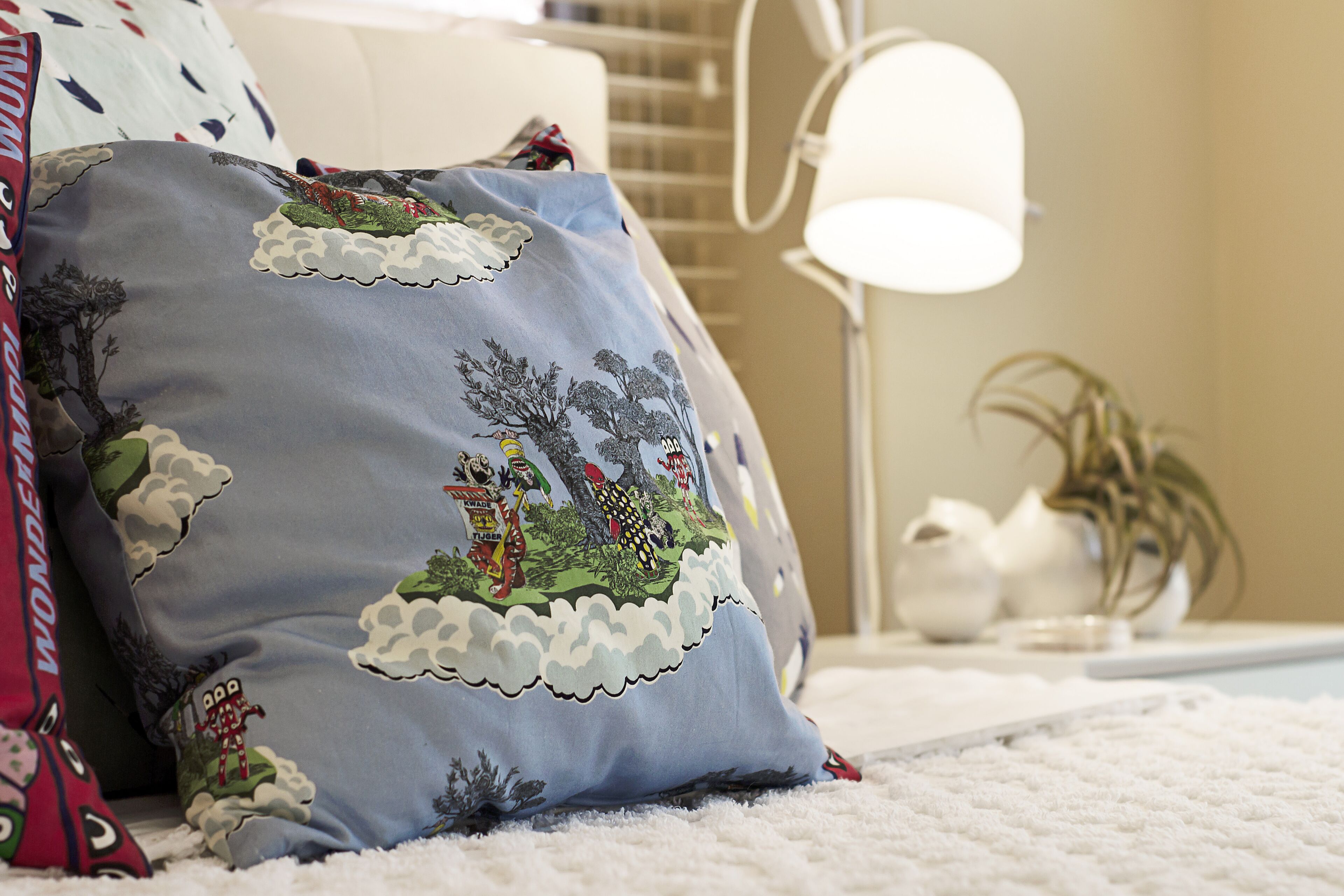 A bedroom with a white bed, a lamp, and decorative pillows.