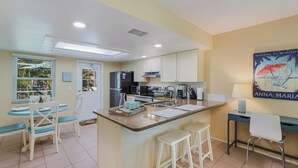 A modern kitchen with white cabinets, a central island with stools, a refrigerator, a microwave, and a coffee maker. - Island Hideaway East: 5 Minute Walk to Beach, Private Pool by Anna Maria Life Vacation Rentals (Holmes Beach)