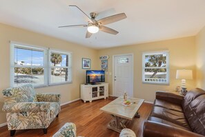 A living room with a ceiling fan, a television, a coffee table, a sofa, and two windows with blinds.
