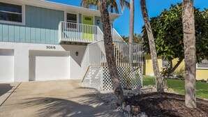 A two-story house with a balcony, a garage, and a well-maintained lawn. - Island Hideaway East: 5 Minute Walk to Beach, Private Pool by Anna Maria Life Vacation Rentals (Holmes Beach)
